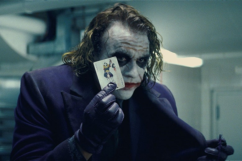 Heath Ledger as the Joker in The Dark Knight. He wears smeared, clown-like makeup and holds a playing card.